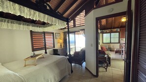 A bedroom with a bed, a desk, and a chair. There is a window with blinds and a view of the outside. - Tropical Orchid-Just For Two-WINTER STORM SALE- Hot Tub (Cruz Bay)