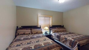 Quarto com duas camas, uma janela com persianas, mesa de cabeceira com abajur e luminária no teto.