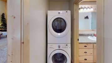 A laundry room with two stacked washing machines, a wooden cabinet, and a small mirror.