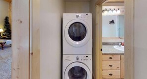 A laundry room with two stacked washing machines, a wooden cabinet, and a small mirror.