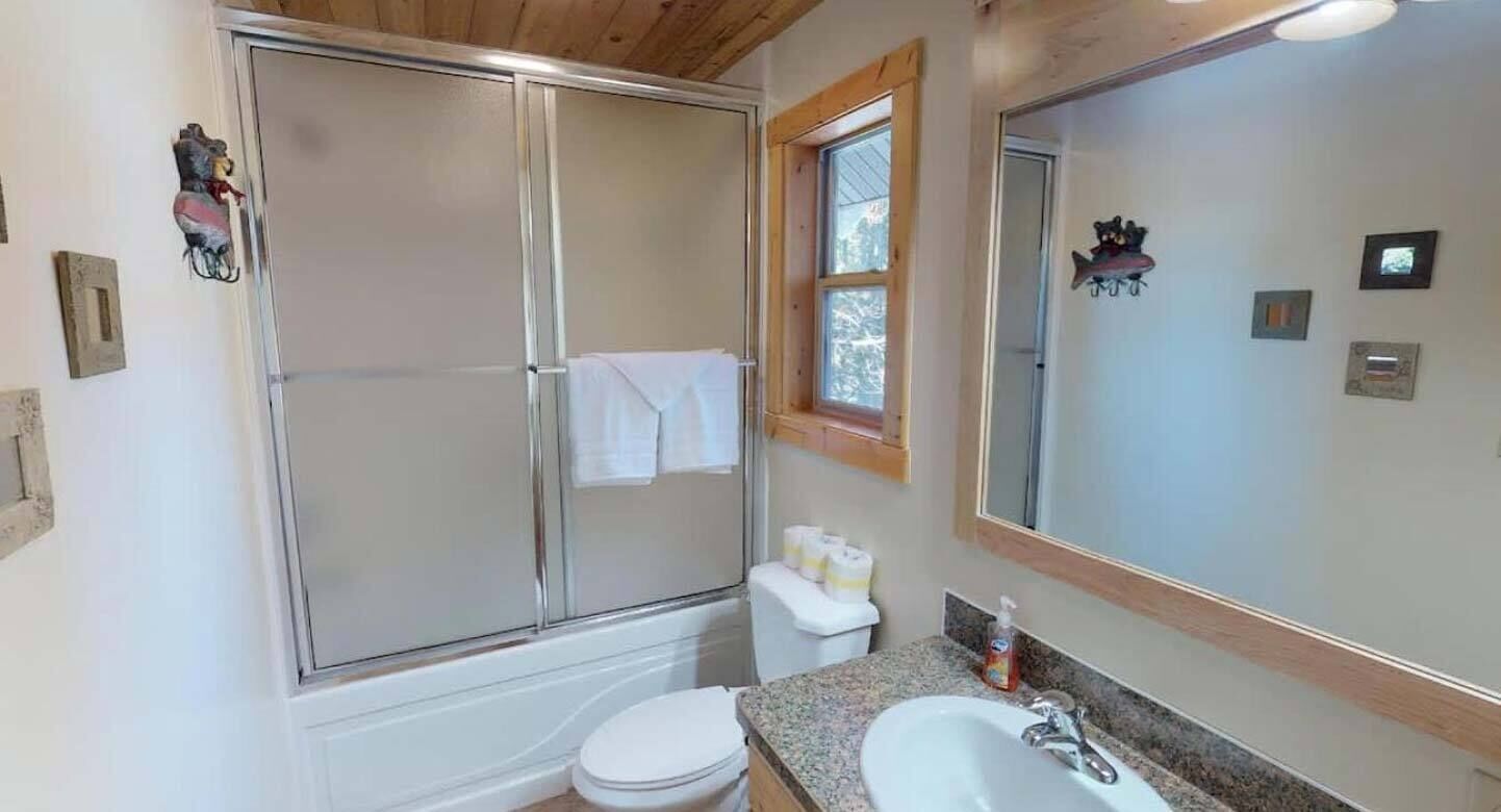 Un baño con ducha de vidrio, inodoro, lavamanos y un espejo grande.