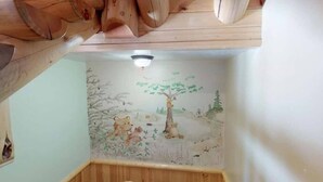 Um quarto com teto de madeira, parede branca com um mural e chão de madeira.