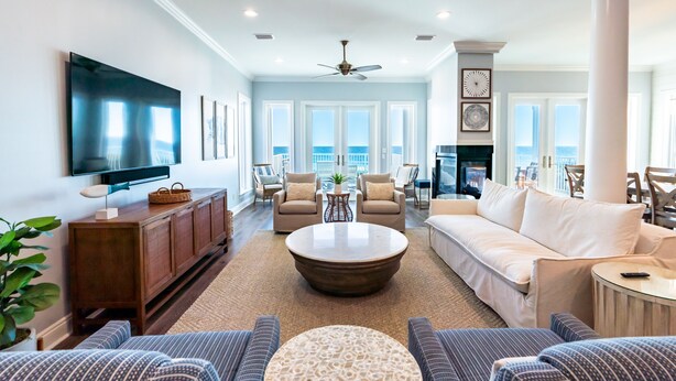 A spacious living room with a large flat-screen TV, comfortable seating, a fireplace, and a view of the ocean.