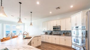 A modern kitchen with white cabinets, a marble countertop, stainless steel appliances, and pendant lighting.
