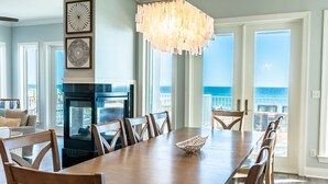 A spacious dining area with a long wooden table, multiple chairs, a chandelier, and a fireplace.
