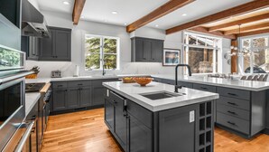 Une cuisine moderne avec des meubles de couleur sombre, un grand îlot central et un plafond en bois.