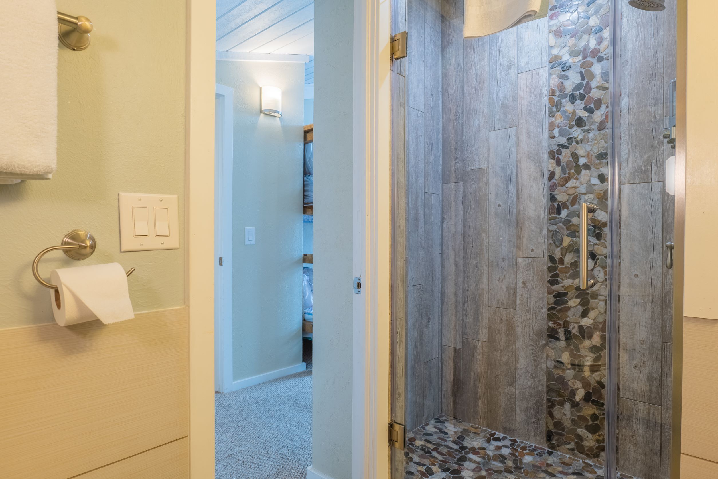 A bathroom with a shower, a toilet paper holder, and a towel rack.
