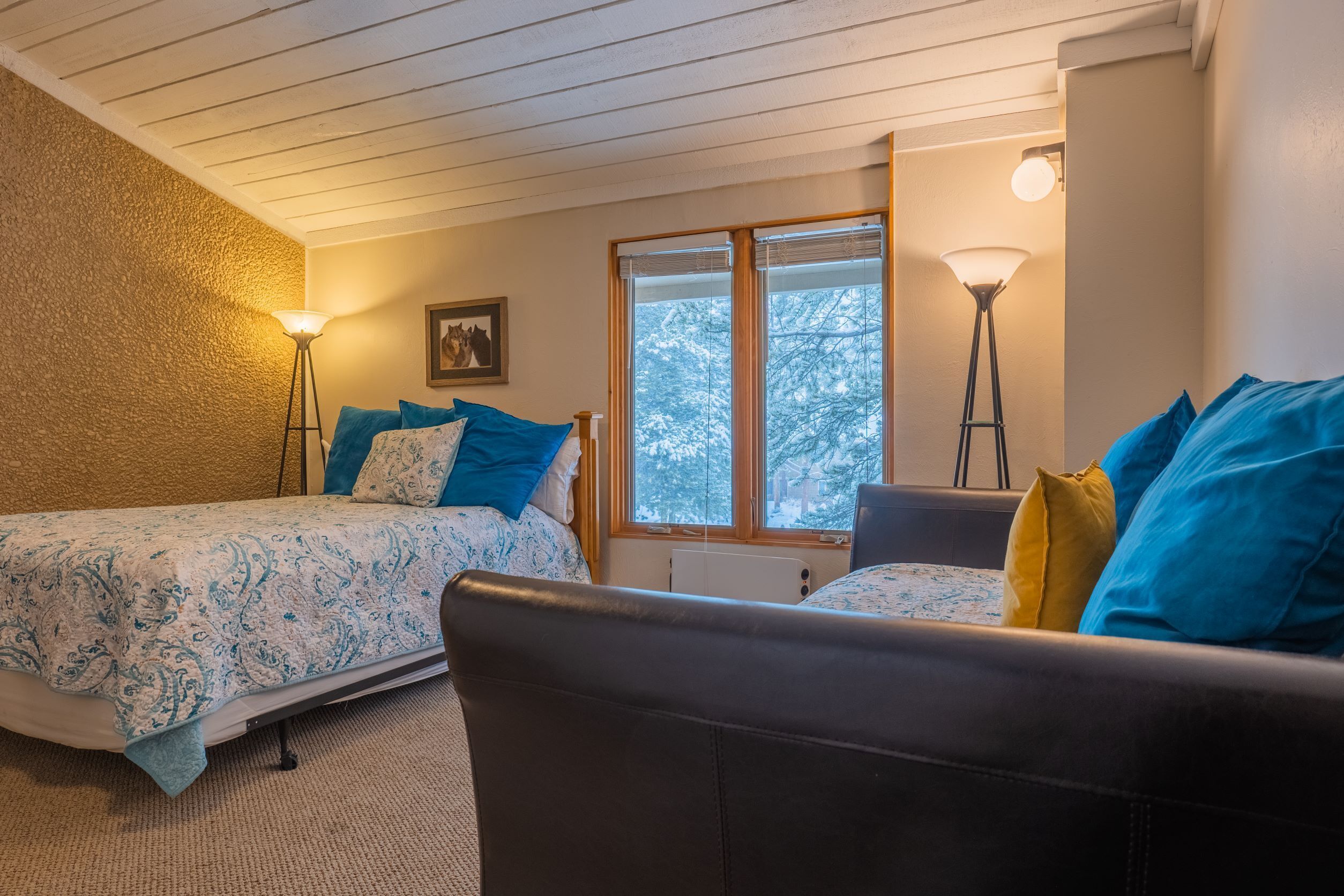 A cozy room with two beds, a couch, and a large window with a view of trees.