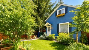 Una casa blu con un giardino curato, una recinzione in legno e un piccolo deposito.