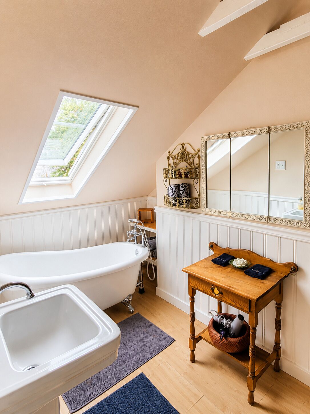 Une salle de bain avec une baignoire sur pieds, un meuble-lavabo avec un miroir et une fenêtre au-dessus du lavabo.