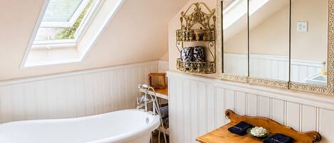 Une salle de bain avec une baignoire sur pieds, un meuble-lavabo avec un miroir et une fenêtre au-dessus du lavabo.