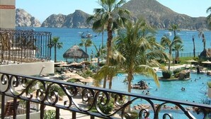 Zona de piscina con palmeras, una montaña al fondo y barcos en el agua.