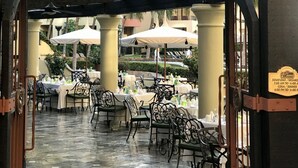 Un espacio al aire libre con mesas y sillas, un letrero que dice 'La Estancia Restaurante' y una campana sobre la entrada.