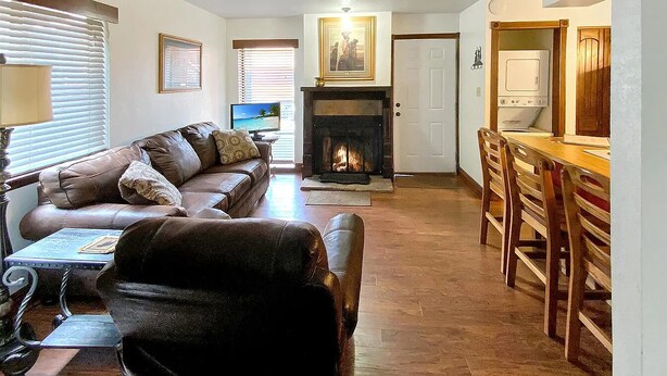A living room with a fireplace, a sofa, a dining table with chairs, and a kitchen area with appliances.