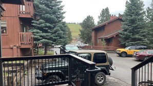 A wooden deck with a black railing, a parked SUV, and a yellow car in a residential area with houses and trees.