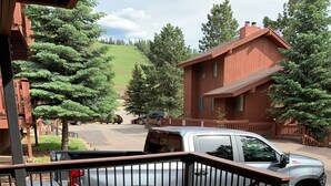 A wooden deck with a metal railing, a parked SUV, and a residential building in the background.