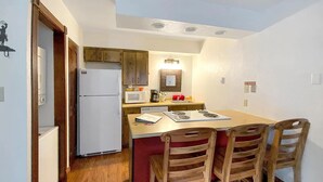A compact kitchen with a refrigerator, microwave, and stove. There is a dining table with four chairs and a small island with a sink.