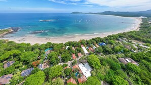 Eine Luftaufnahme einer Küstenregion mit Strand, Booten und Wohnhäusern, umgeben von viel Grün.