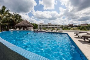 A swimming pool with lounge chairs, a thatched-roof hut, and a building in the background. - 1-Bedroom Unit With Convenient Access to the Pool and Beach (Cozumel)