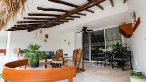 An outdoor seating area with wooden furniture, a thatched roof, and a sliding glass door leading to a covered patio. - 1-Bedroom Unit With Convenient Access to the Pool and Beach (Cozumel)