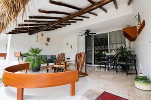 Un espace extérieur aménagé avec du mobilier en bois, un toit de chaume et une porte-fenêtre coulissante donnant sur un patio abrité.