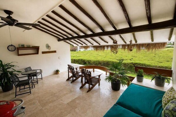 A covered patio with a ceiling fan, outdoor seating, potted plants, and a view of a grassy area. - 1-Bedroom Unit With Convenient Access to the Pool and Beach (Cozumel)
