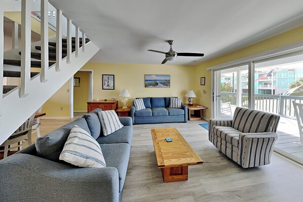 A living room with a sofa, armchair, and coffee table, a staircase, and a balcony with a view.