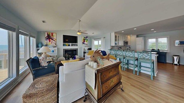 A spacious living area with a fireplace, a dining area with teal chairs, and a kitchen with white cabinets. - The Salty Spot | Family Favorite Oceanfront Retreat w/Beach Access (Surf City)