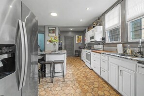 A kitchen with a stainless steel refrigerator, white cabinets, a marble countertop, and a hexagonal tile floor.