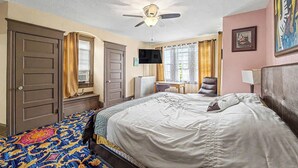 Un dormitorio con cama, escritorio, silla, ventilador de techo y televisor.