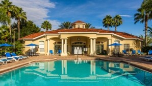 A hotel with a swimming pool, palm trees, and a Mediterranean-style building.
