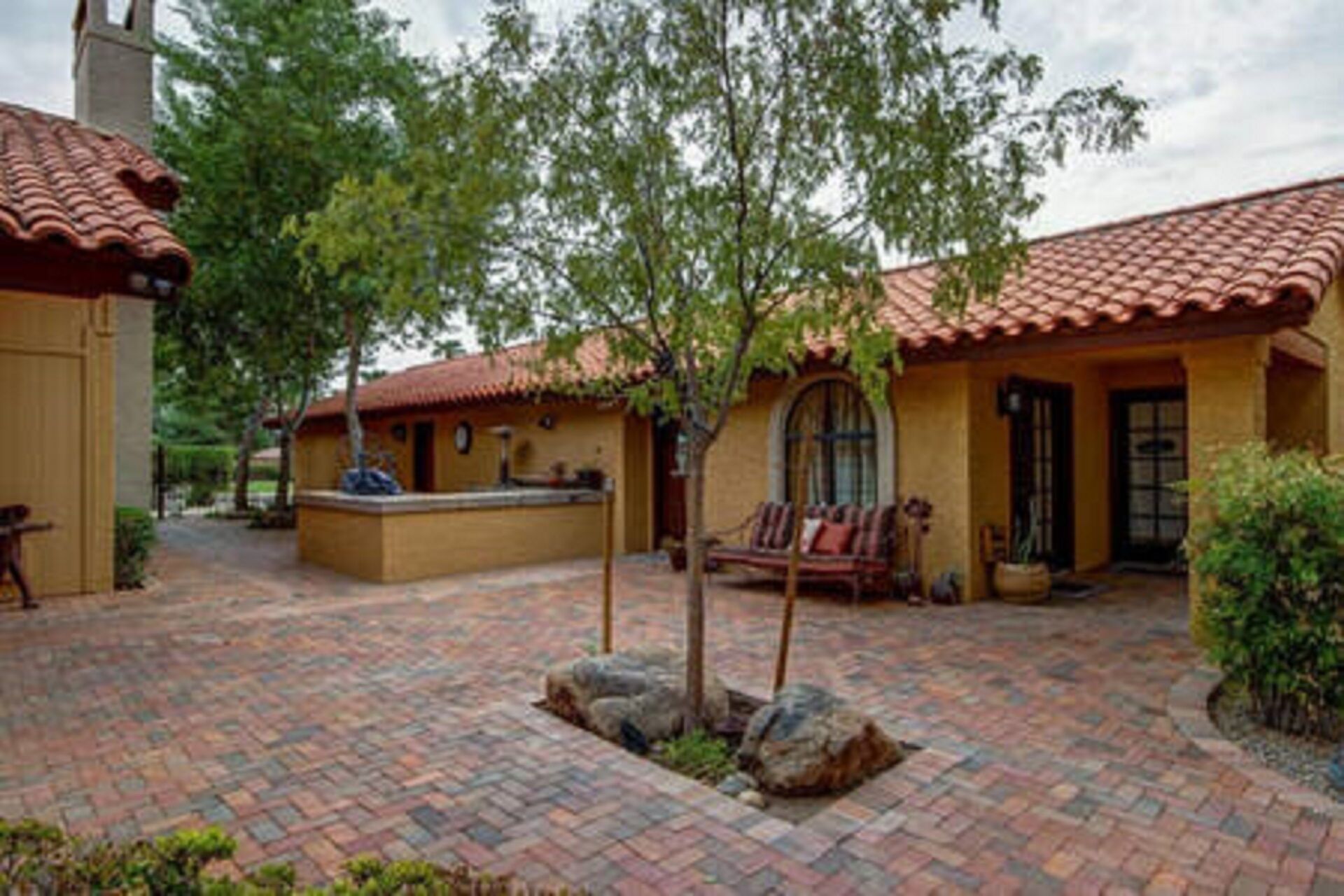 A courtyard with a tiled floor, a bench, and a small tree.