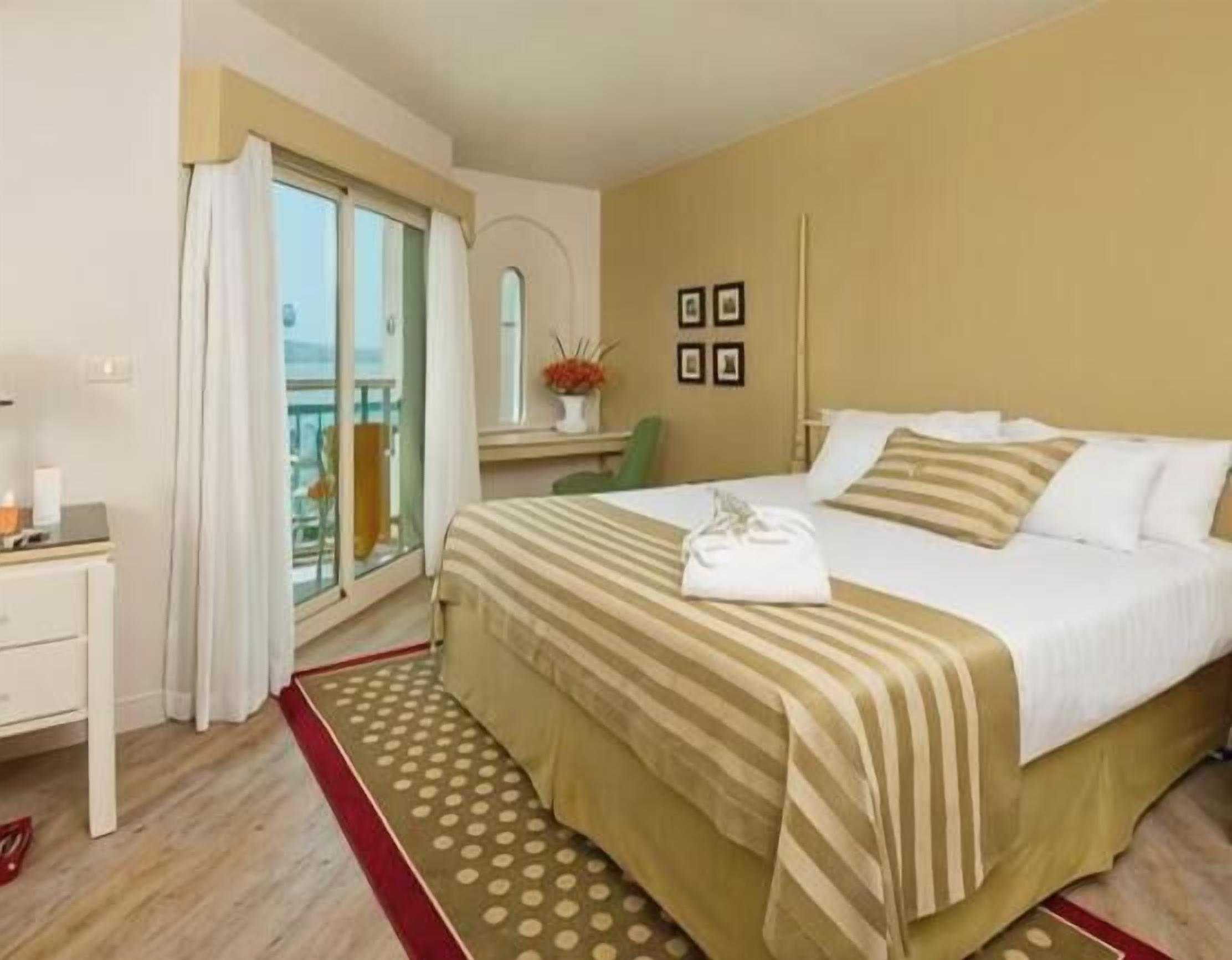 A hotel room with a bed, a desk, a chair, a window with curtains, and a view of the outdoors.
