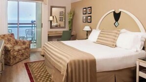 A hotel room with a bed, a chair, a desk, a lamp, and a view of the sea. - Herods Palace Hotels & Spa Eilat (Eilat)