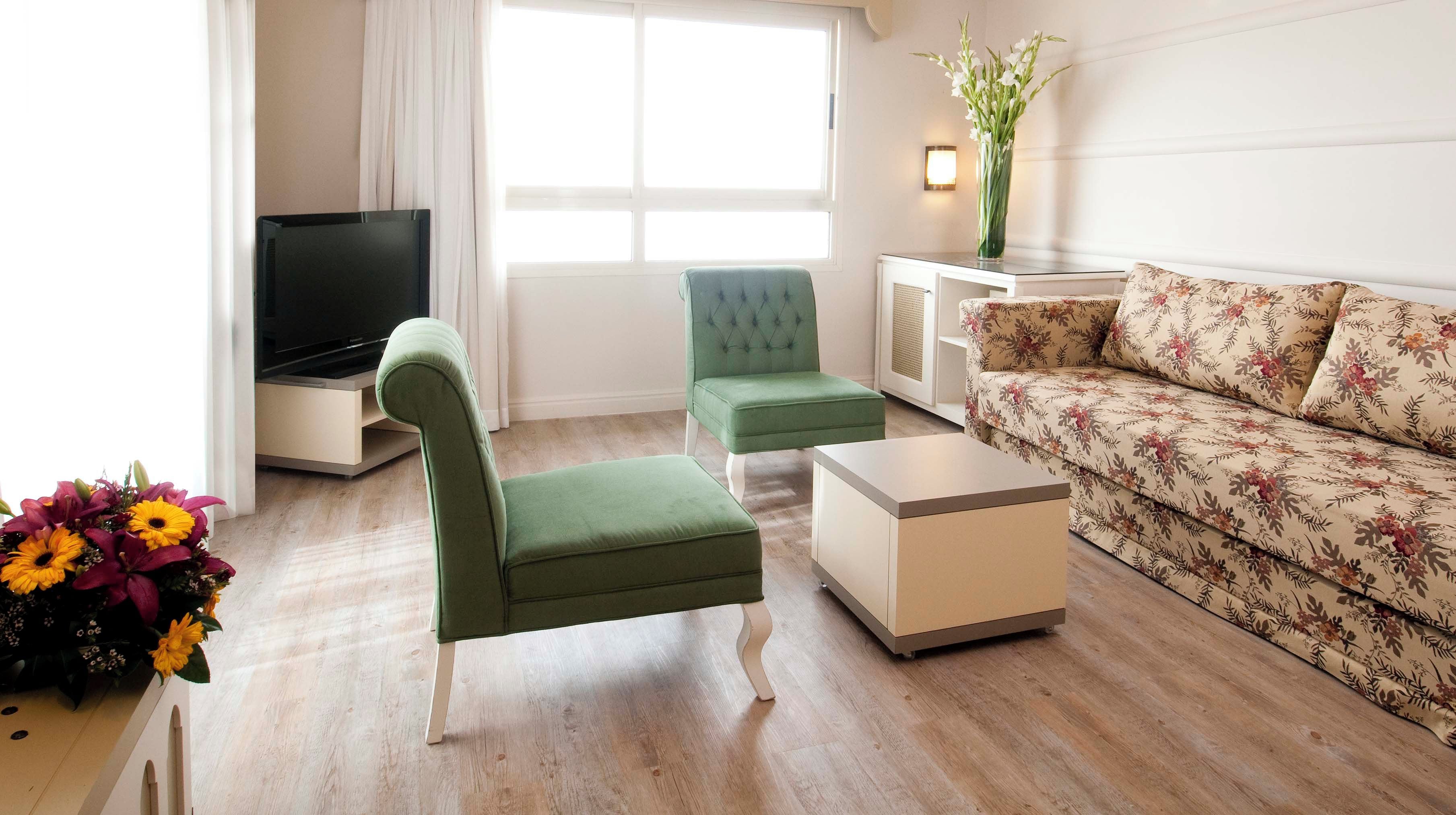 Ein Wohnzimmer mit einem grünen Sessel, einer Couch, einem Fernseher und einem blumigen Sofa.