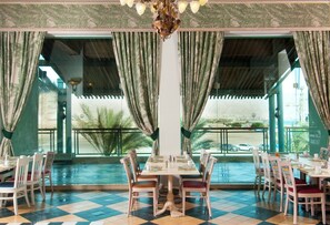 A restaurant with a pool view, multiple dining tables, and tropical-themed curtains. - Herods Palace Hotels & Spa Eilat (Eilat)