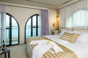 A hotel room with a bed, a nightstand, a lamp, and a view of the sea through arched windows. - Herods Palace Hotels & Spa Eilat (Eilat)