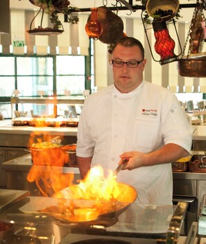 A chef in a professional kitchen with a large pot on the stove, flames, and various cooking utensils. - Herods Palace Hotels & Spa Eilat (Eilat)