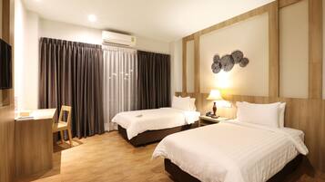 A hotel room with two beds, a desk, a chair, a TV, and an air conditioning unit.