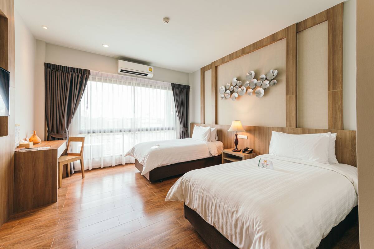 A hotel room with two beds, a desk, a chair, and a large window with curtains.