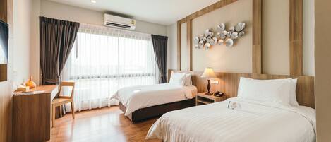 Habitación de hotel con dos camas, un escritorio, una silla y un ventanal con cortinas.