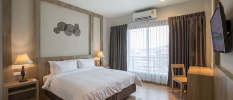 Habitación de hotel moderna con una cama grande, dos mesitas de noche con lámparas, un televisor de pantalla plana montado en la pared y una ventana con cortinas.