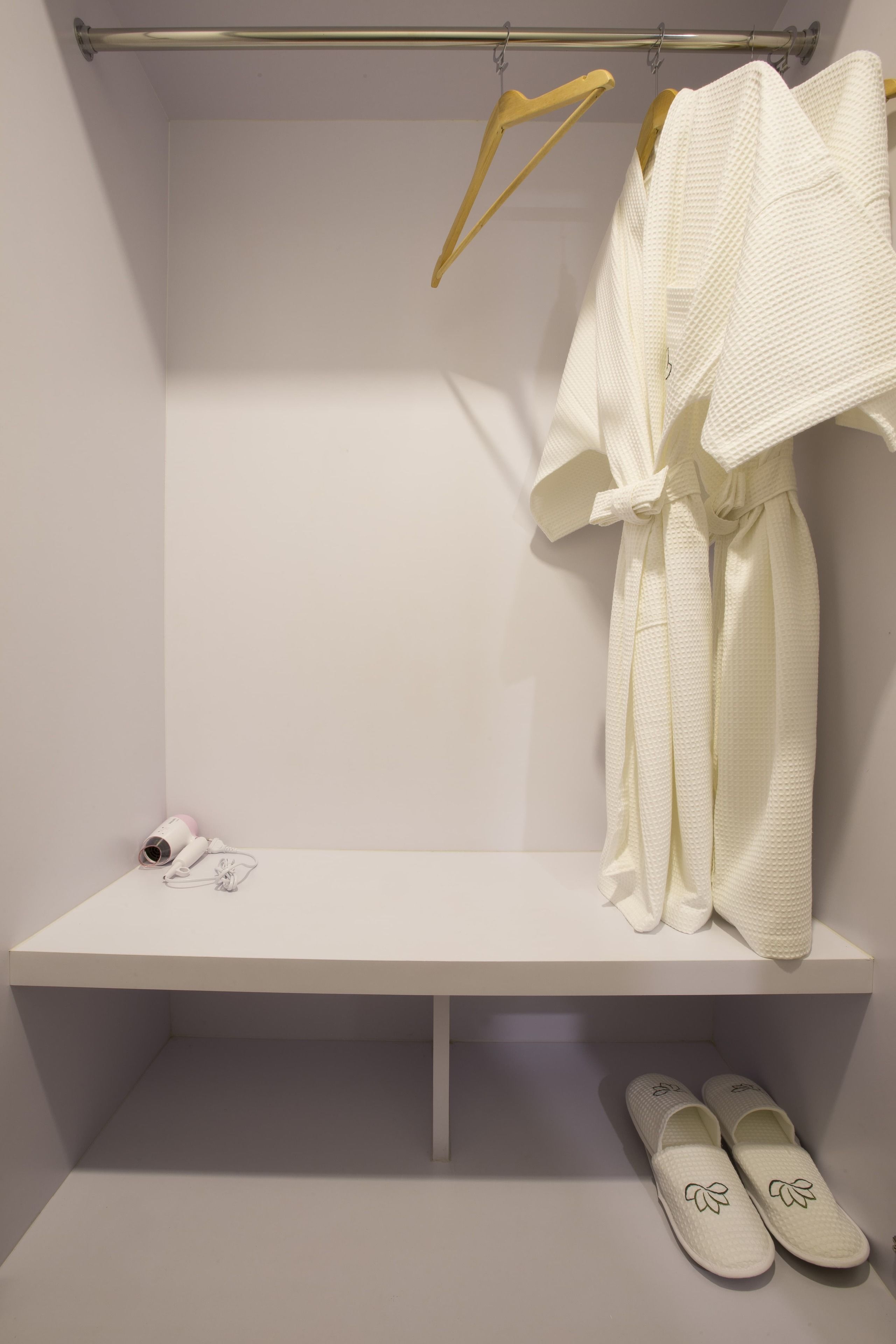 Un baño blanco con una bata colgada en un perchero, una toalla y zapatillas en el suelo.