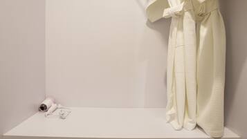 A white bathroom with a robe hanging on a rack, a towel, and slippers on the floor.