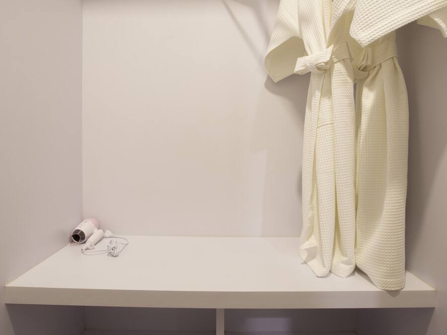 Un baño blanco con una bata colgada en un perchero, una toalla y zapatillas en el suelo.