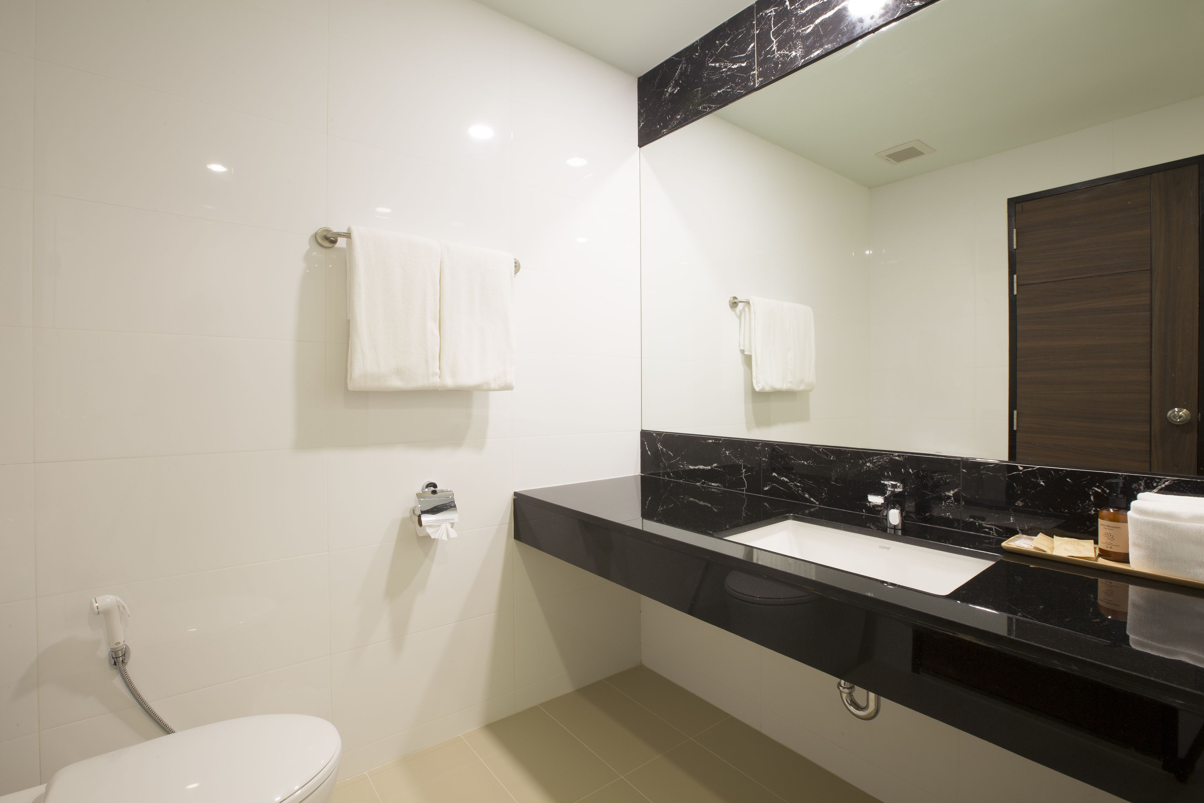 Un baño moderno con lavamanos de mármol negro, azulejos blancos y una puerta de madera.