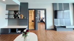 A modern living room with built-in shelves, a flat-screen TV, and a dining area. - Civilize Hotel (Udon Thani)