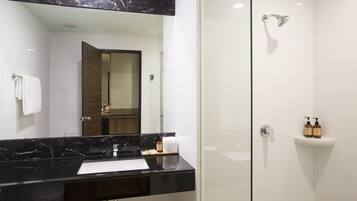 Un baño moderno con encimera de mármol negro, cabina de ducha de vidrio y lavabo blanco.