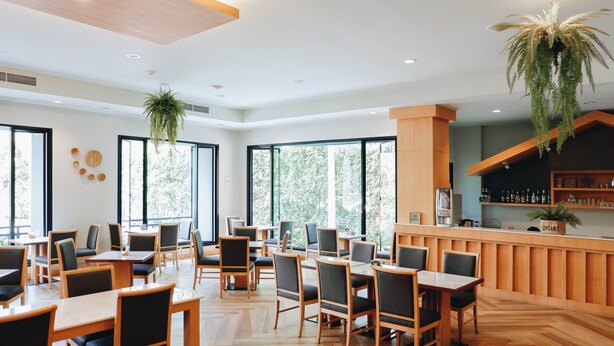A modern restaurant with wooden tables and chairs, large windows, and a bar area. - Civilize Hotel (Udon Thani)