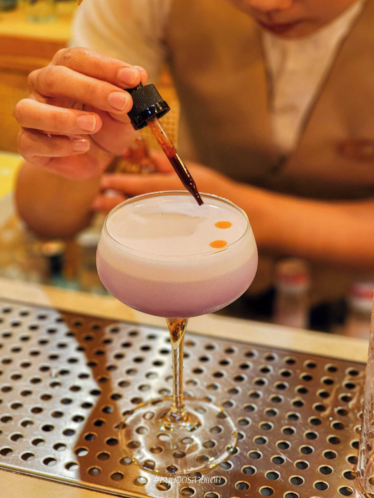 Un barman sirviendo una bebida en una copa de martini sobre una barra de metal perforado.